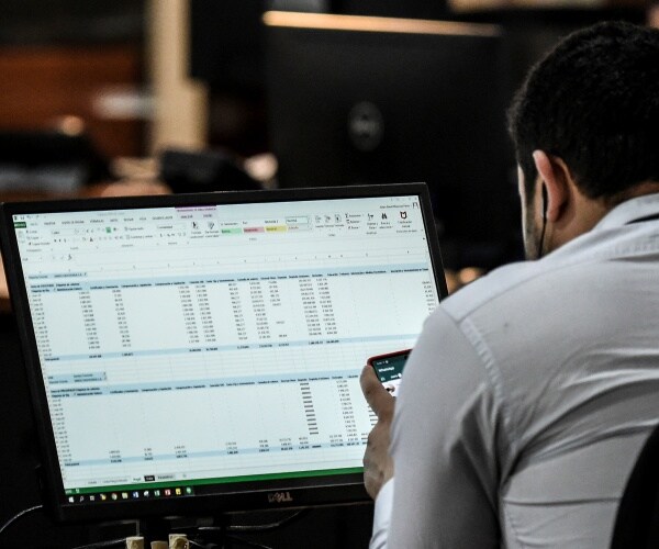 man wearing a gray shirt looking at an excel spreadsheet on a computer