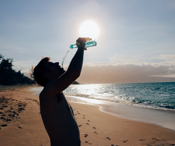 man on beach in sun drinking water from a bottle