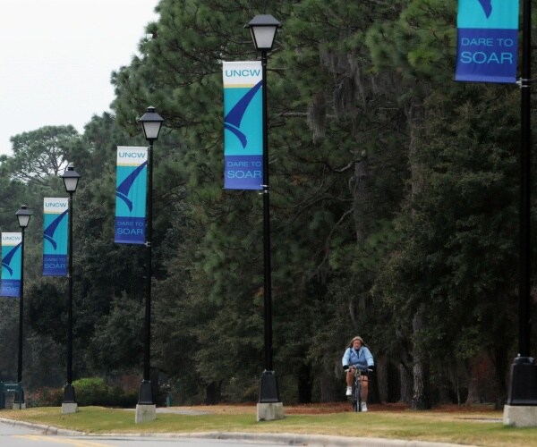 student rides a bike passing by banners saying dare to soar uncw on them