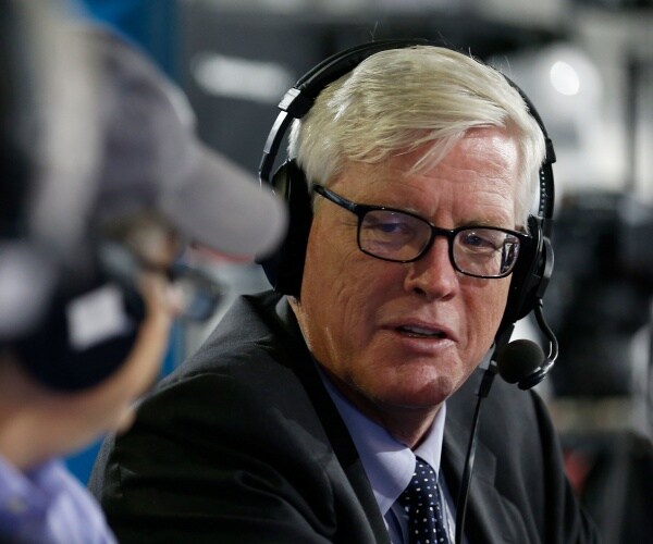 hewitt wearing headphones and a dark gray suit and blue shirt and polka dotted tie