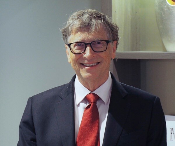 bill gates stands in front of a vase and smiles