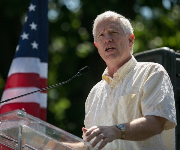 brooks in a light yellow short sleeve shirt speaking outside at a podium