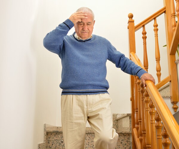 a senior man feeling dizzy standing on the stairs wearing a blue sweater