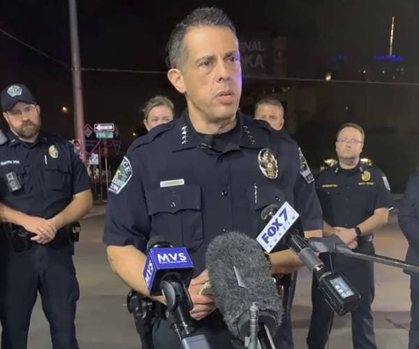 police chief standing in front of a microphone with police officers standing behind him