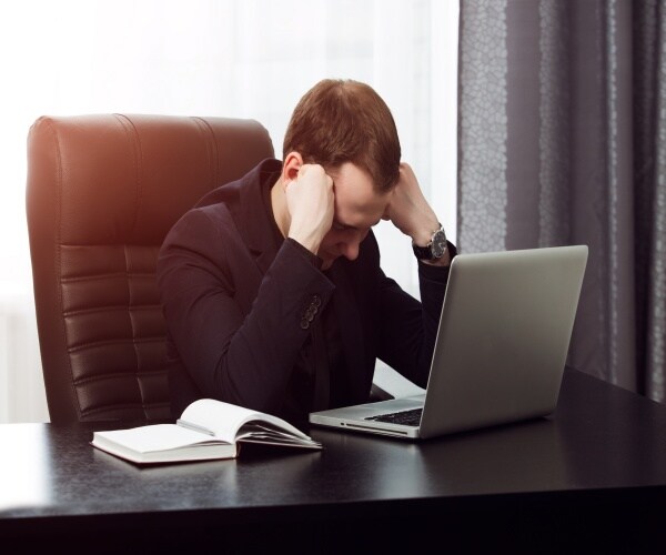 man at work desk with computer with head in hands tired/can't concentrate