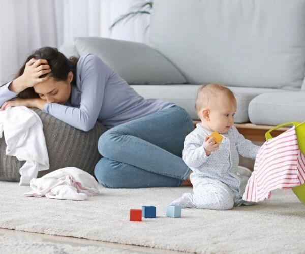 women with head in arms looking depressed, as baby plays nearby