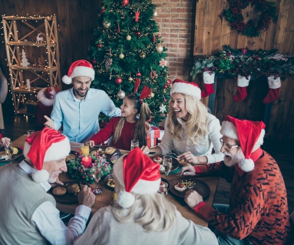 family celebrating christmas wearing santa hats and eating a meal at the table near a christmas tree