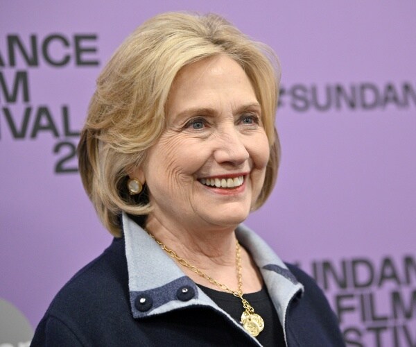 hillary in a navy blue jacket and gold necklace