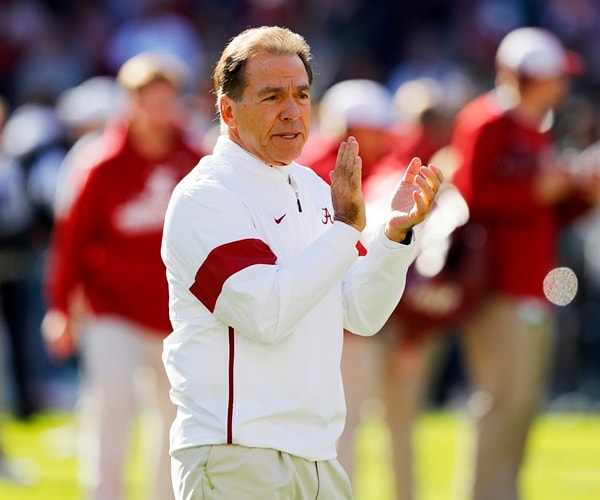 nick saban walks across a football field clapping