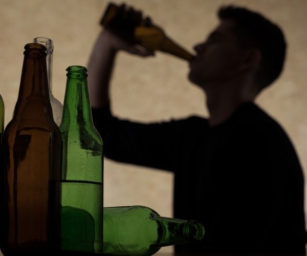 a shadow of young man drinking alcohol from bottle with other bottles on table too