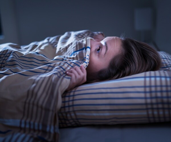 woman in bed with covers up over half her face looking terrified