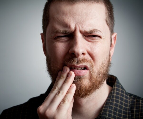 man holding side of face, wincing, with tooth pain