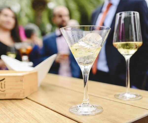 a glass of wine, a glass of an alcoholic drink on table in foreground, people at party in background