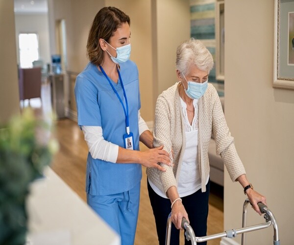 a nurse walking with an elderly woman using a walker in a nursing home