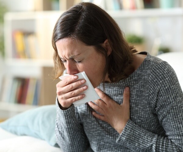 woman in gray sweater coughing into a napkin