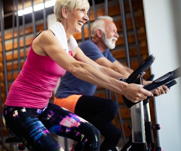 older man and woman on spin bikes in gym