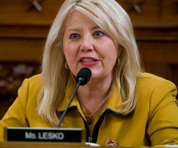 lesko in a mustard yellow coat speaking into a microphone