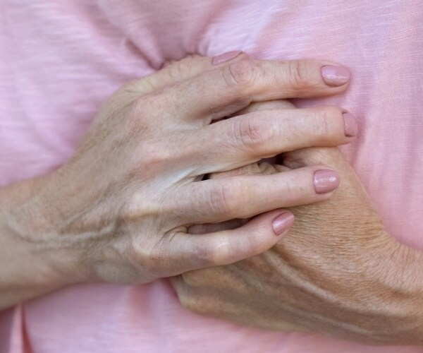 older woman in pink shirt holding her chest area in pain