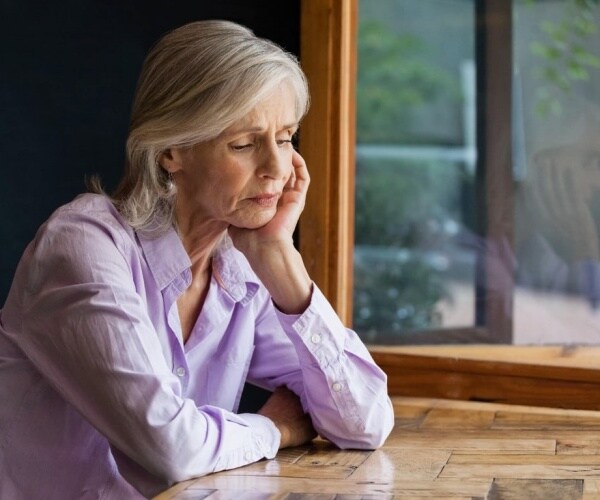 older woman sitting at table by window looking sad