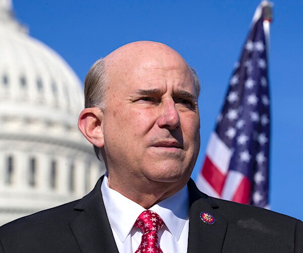 louie gohmert looks to his left with capitol hill and the american flag in the background