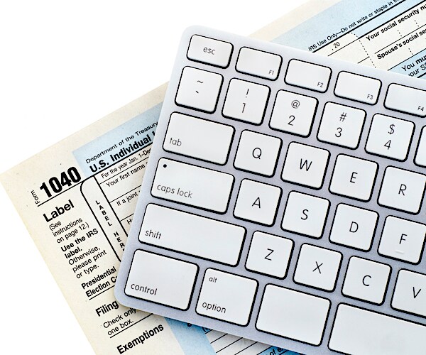 the 1040 tax filing forms lay on a white table under and eye mack wireless keyboard