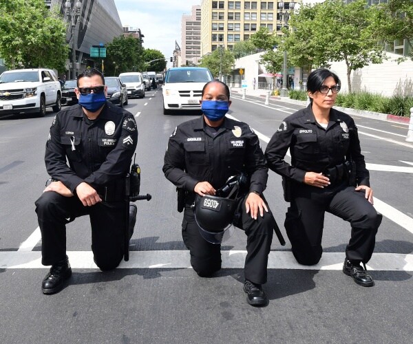 lapd officers in black uniforms kneel in the middle of the road with two wearing blue face masks