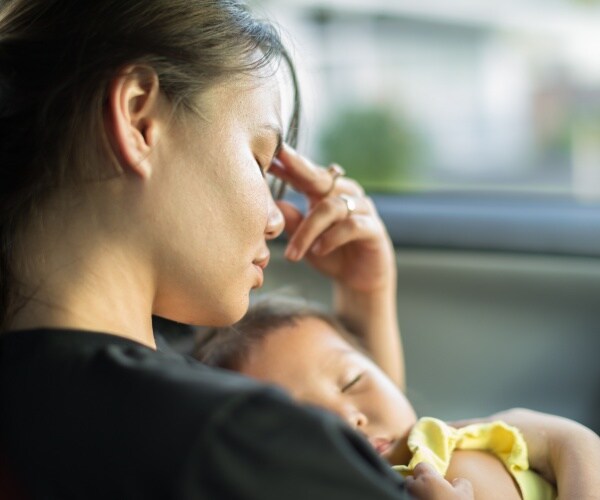 woman with postpartum depression looking overwhelmed holding baby in car