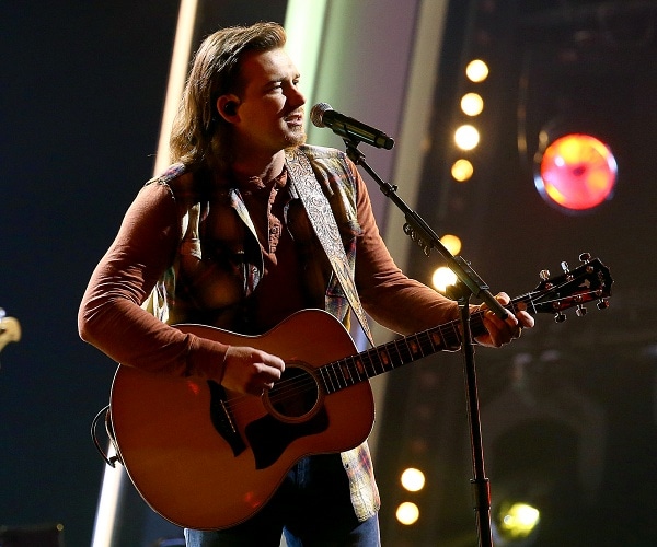 morgan wallen plays guitar and sings into mic onstage