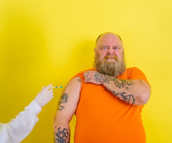 overweight man with beard and tattoos making a doubtful face while arm of healthcare worker giving vaccine