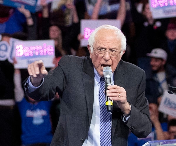 bernie sanders speaks at a mic during a rally with supporters