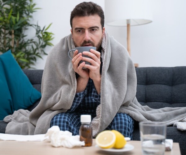 man on couch with blanket, tissues, remedies suffering from cold or flu