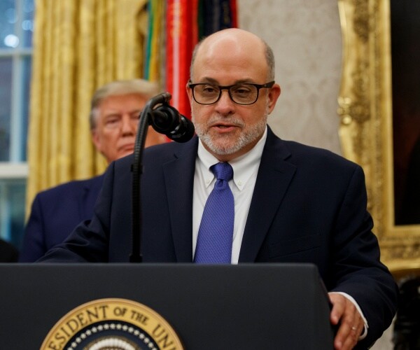 levin in a suit and blue tie speaks with trump behind him