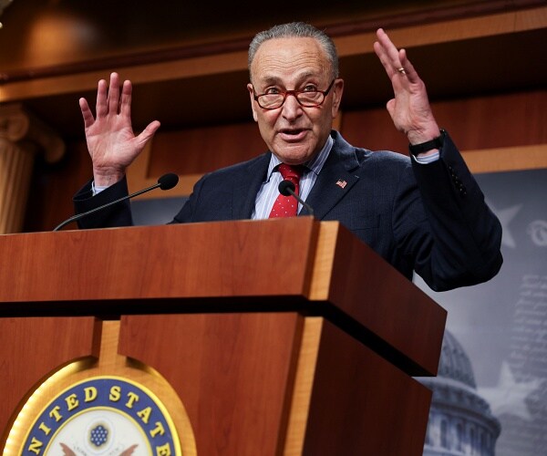 chuck schumer raises his hands as he speaks at news conference