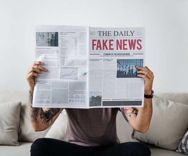 man sitting on couch reading newspaper that says fake news