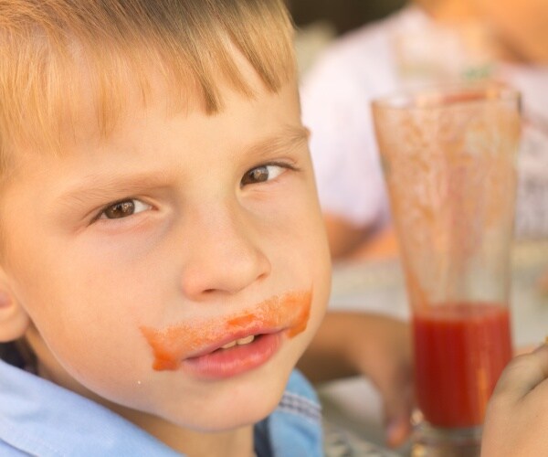 boy drinking tomato juice, with some on his face