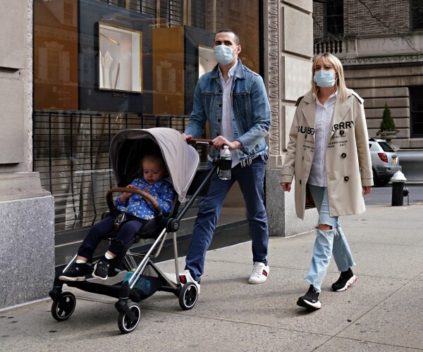 a man and woman wear masks and push their daughter in a stroller on an nyc sidewalk