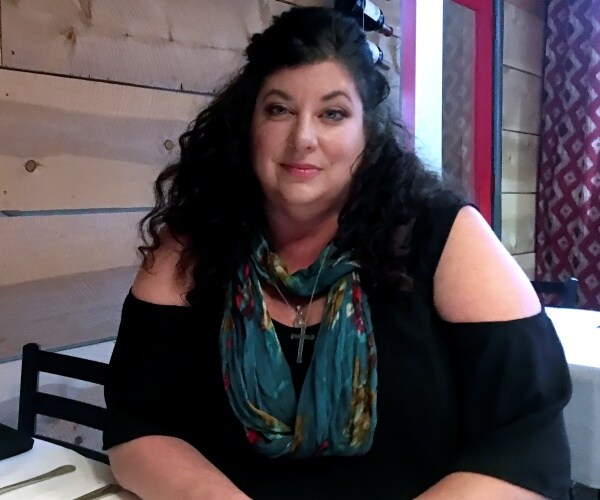 tara reade in a black top and blue and green patterned scarf sitting at a restaurant table