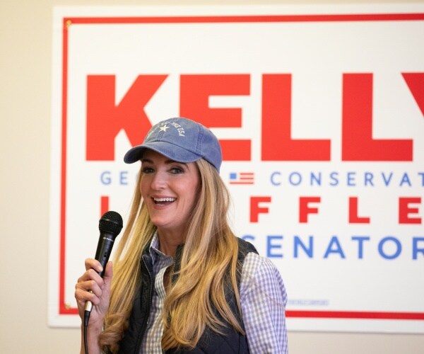 loeffler in a baseball cap speaking in front of a campaign sign