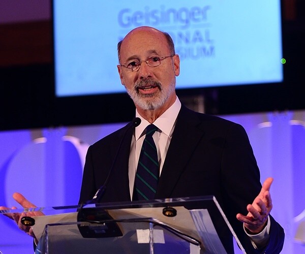 tom wolf speaks from a podium against a blue neon backgroun