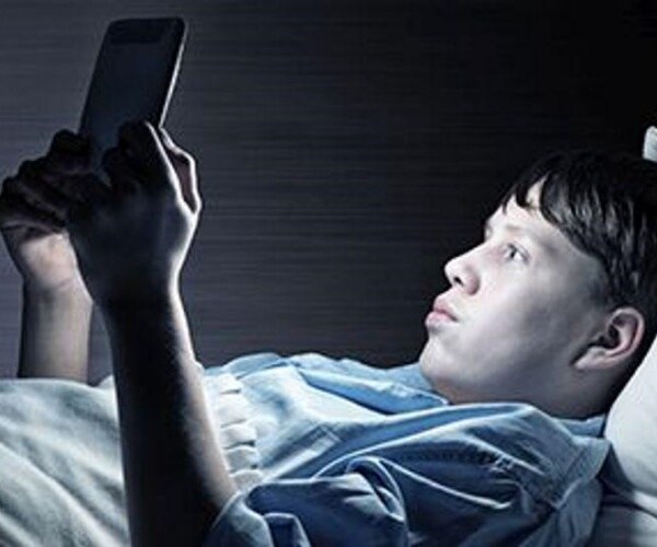 man in bed in dark looking at tablet screen