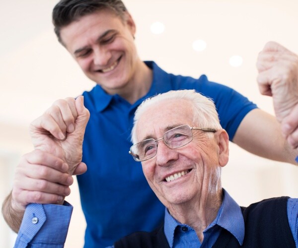 therapist lifting arms of smiling man after stroke