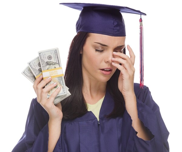 female student in cap and gown, crying while holding piggy bank