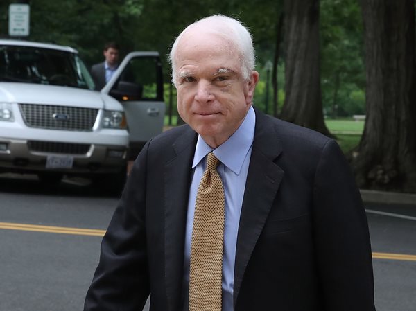 john mccain walks across street and looks to camera.