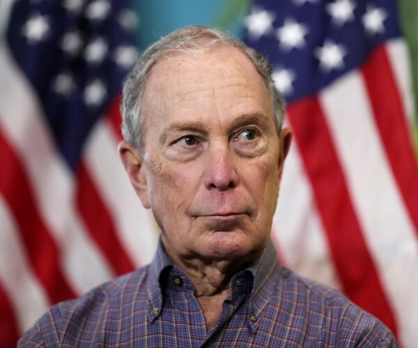 bloomberg in a plaid shirt with us flags behind him