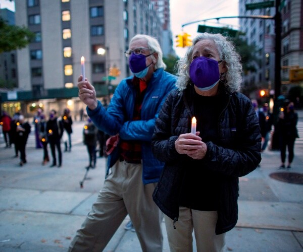 senior couple wearing purple masks hold candles for the vigil