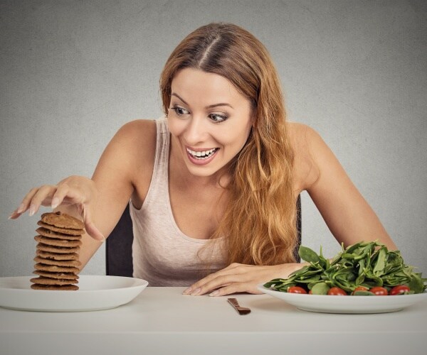 woman choosing a plate of stacked chocolate chip cookies over salad