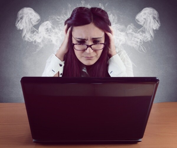 woman at computer with head in hands, smoke coming out her ears, looking stressed