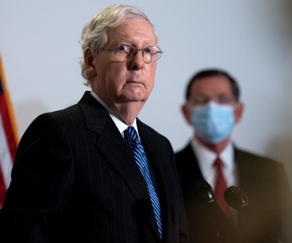 mitch mcconnell stands near a flag and a masked man.