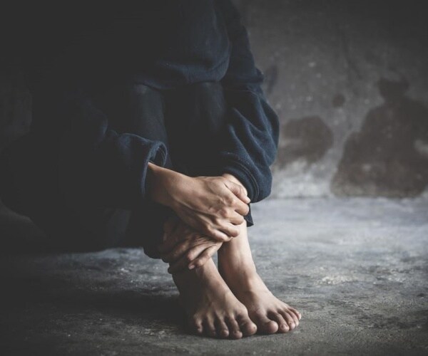 person in despair sitting on floor holding knees, head down