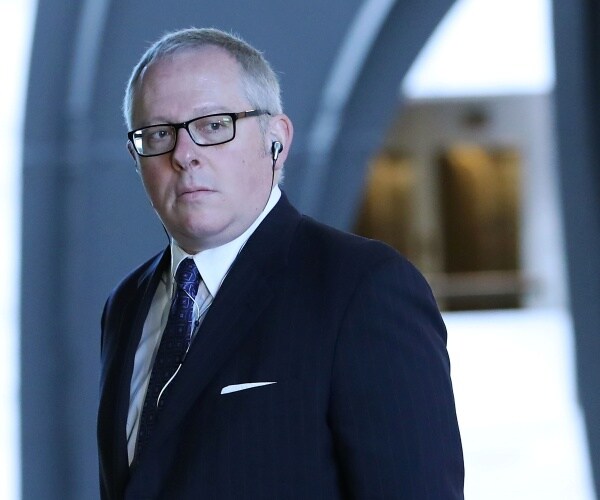 michael caputo in a navy suit and blue tie wearing ear plugs